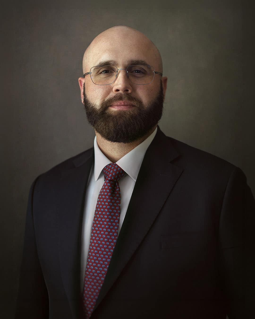 Executive LinkedIn headshot of a business professional in Dubai wearing a navy suit and red tie, photographed in a fine art portrait style.