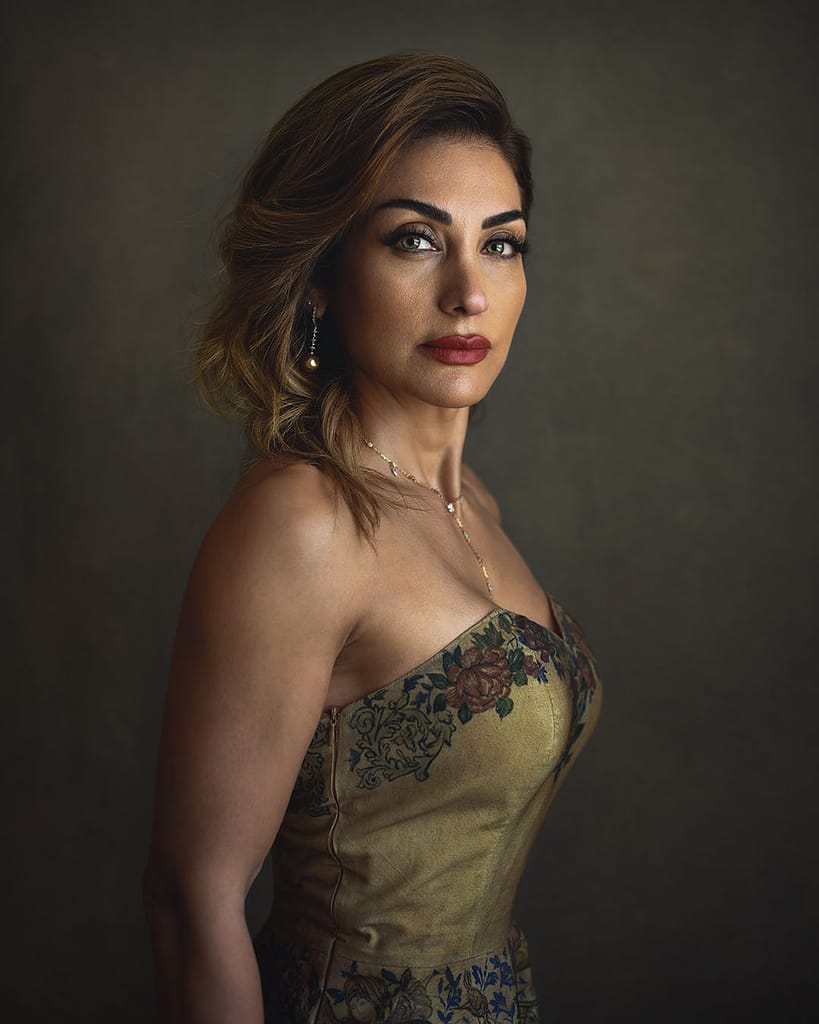 Elegant executive portrait of woman in gold floral dress, side pose, Dubai studio