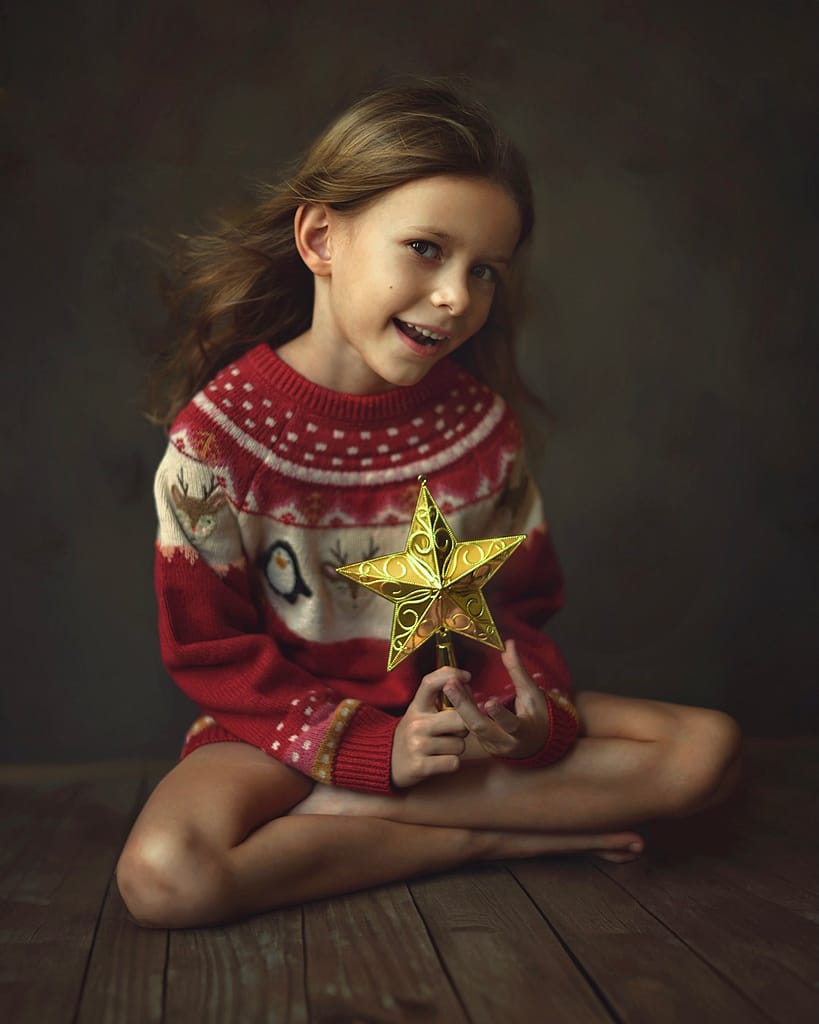 Children's Christmas Photoshoot for 2023. Young girl in a red festive sweater dress holding a decorative golden star.